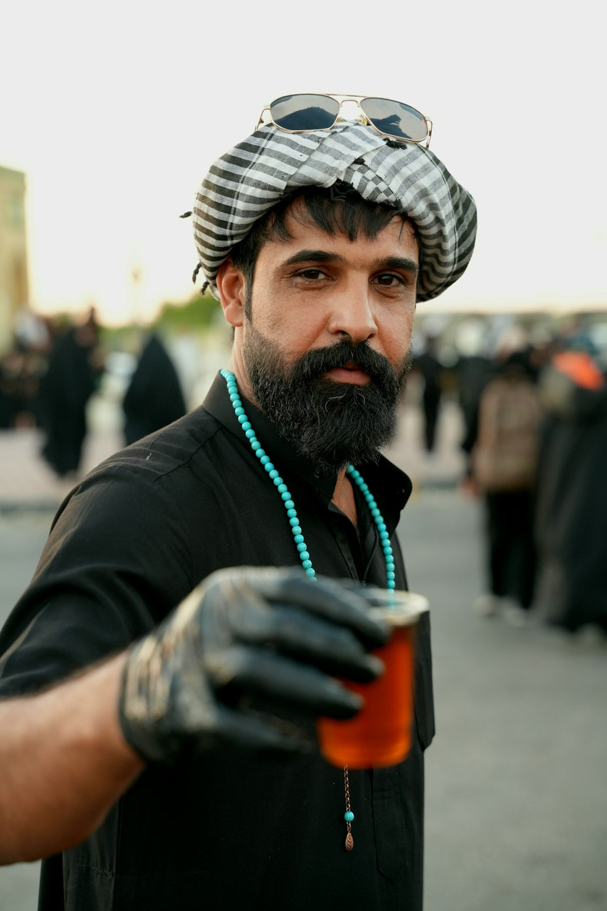 A man with a beard wearing a patterned headscarf and turquoise beads holding a glass, Ultra