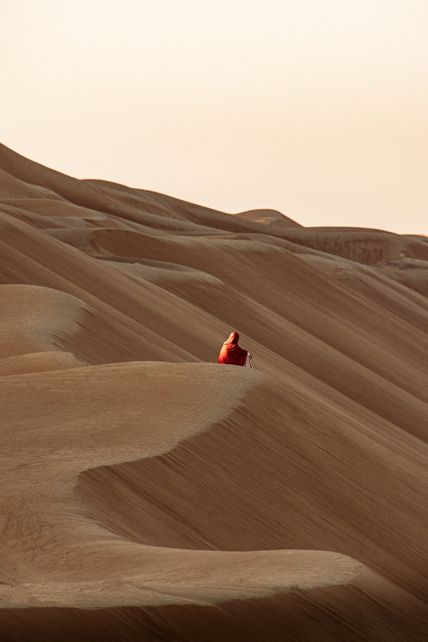 A person in a red cloak on a vast sand dune at golden hour, Ultra