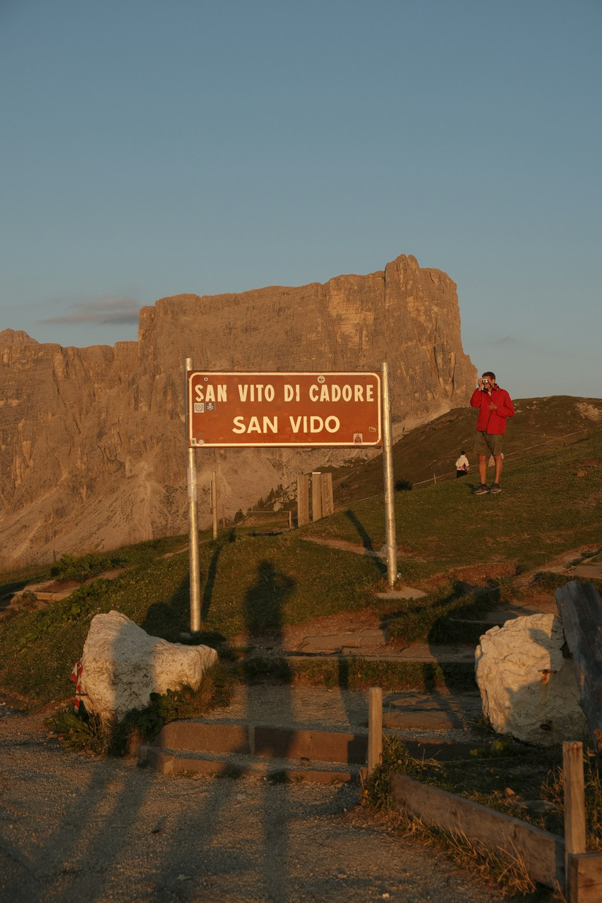 A person in a red jacket photographing a sign for San Vito di Cadore, Ultra