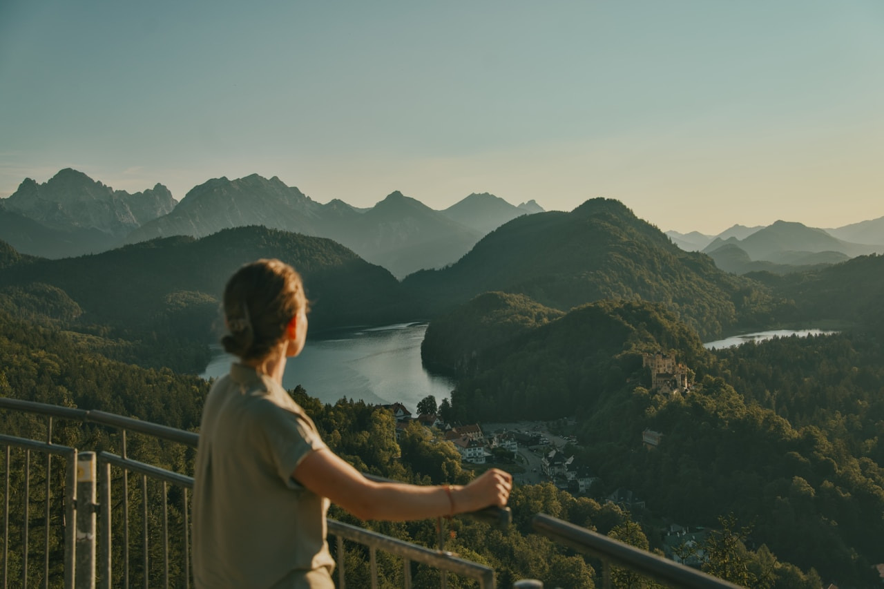 A person looking out over a lake and mountains from a metal railing, Ultra