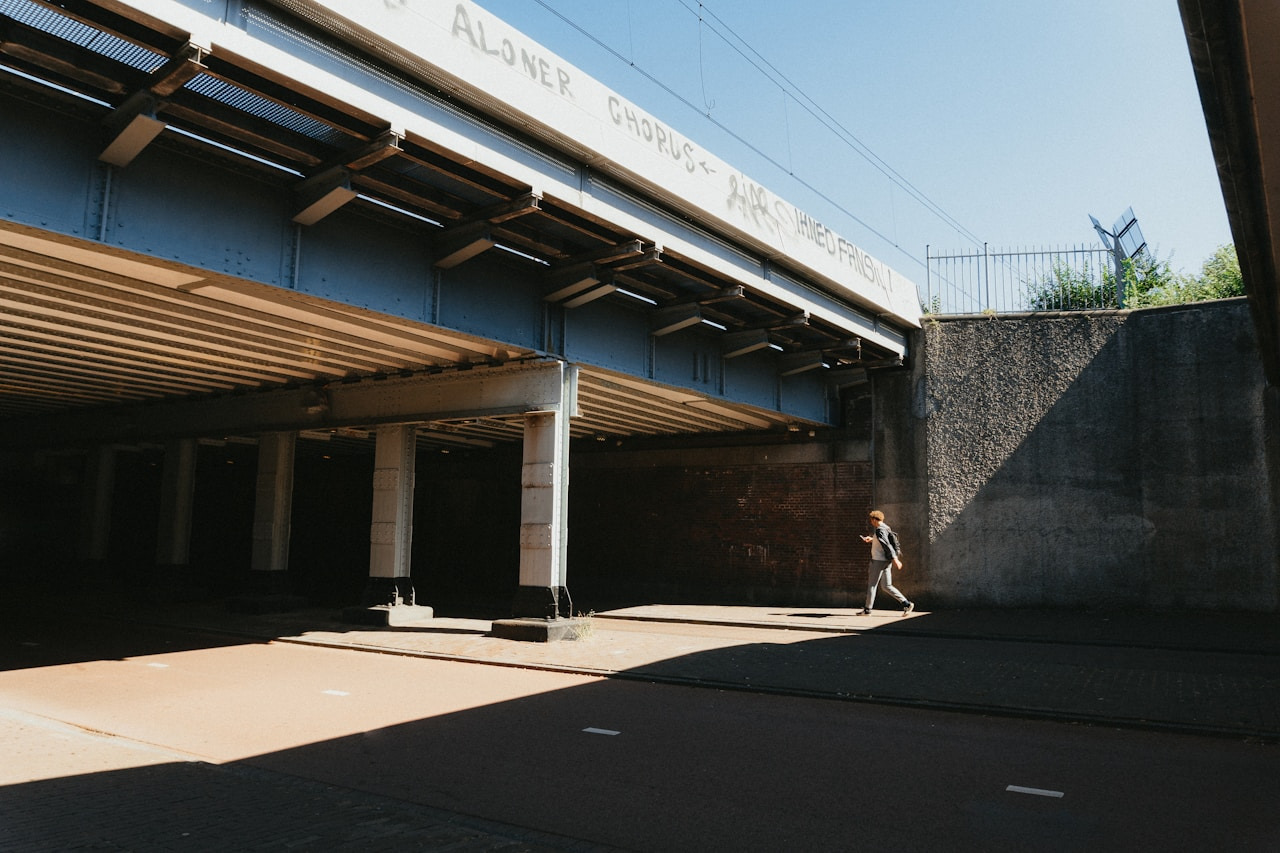 a person walking down a sidewalk under a bridge, Ultra