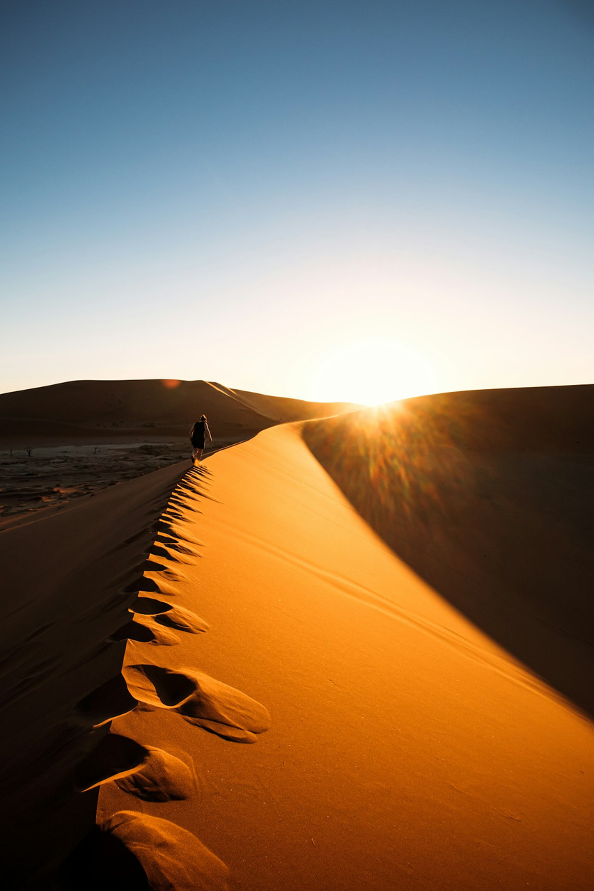A person walks along a desert sand dune at sunset, Ultra