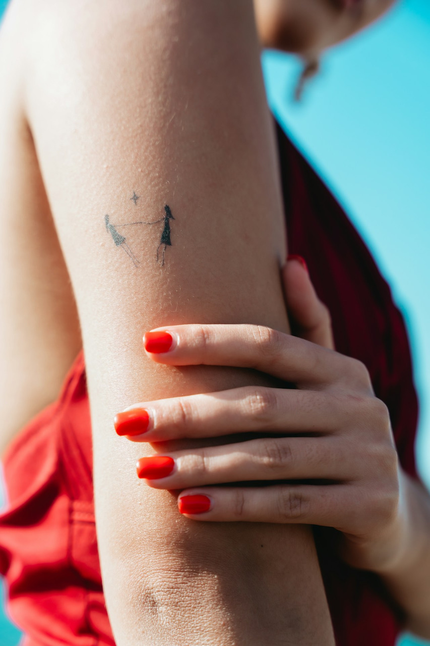 Arm with a minimalist tattoo and vibrant red nail polish, Ultra