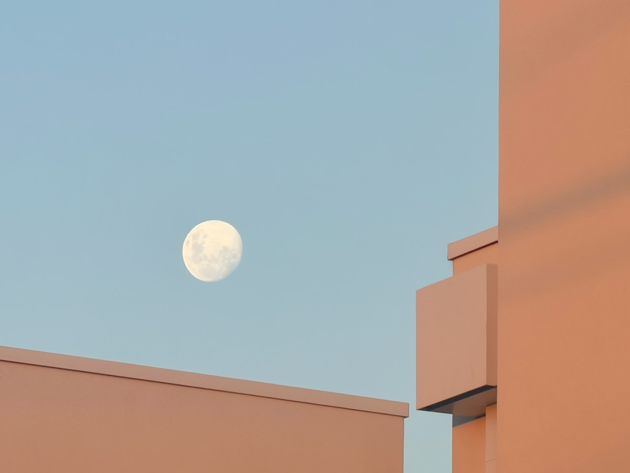 Full moon in a clear blue sky above buildings, Ultra