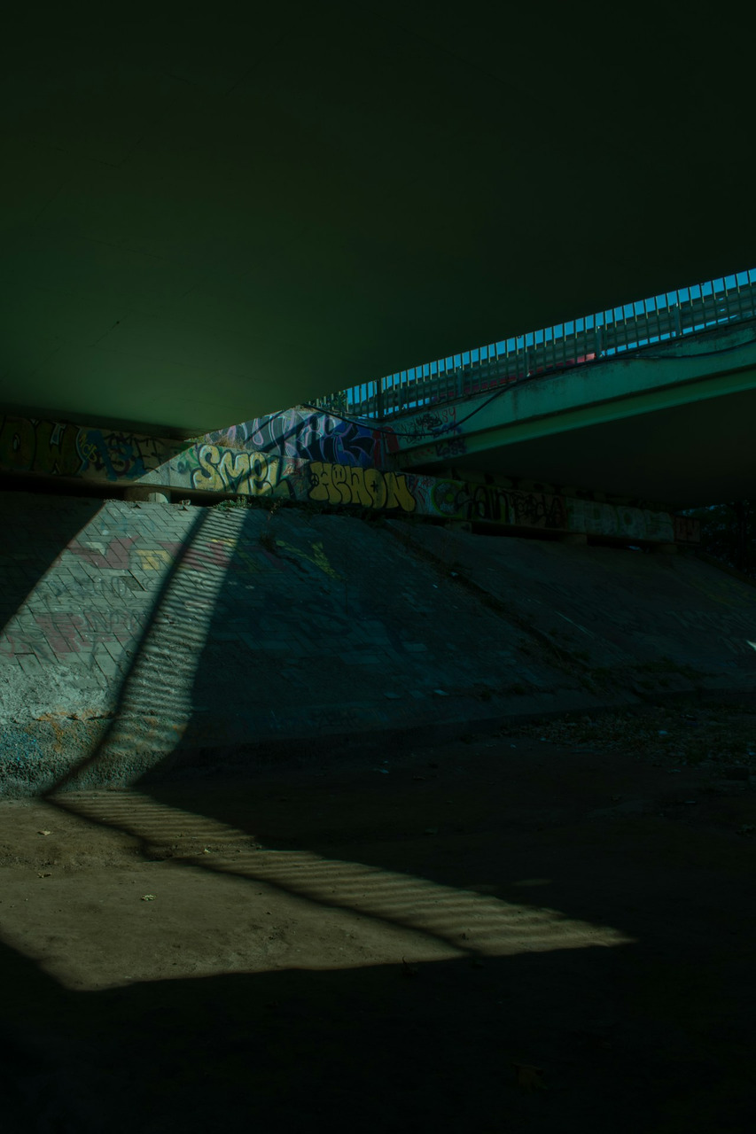 Graffiti on a concrete bridge support with a long shadow cast across the ground, Ultra