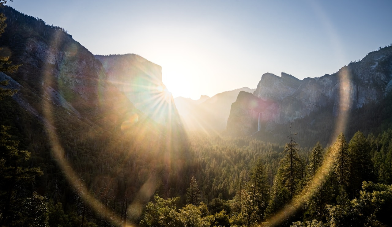 Low sun with lens flare over a forested valley and granite cliffs in Yosemite, Ultra