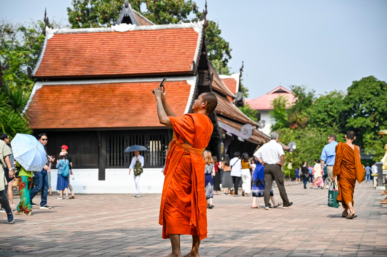 Monk in orange robes raises hands towards temple building, Ultra