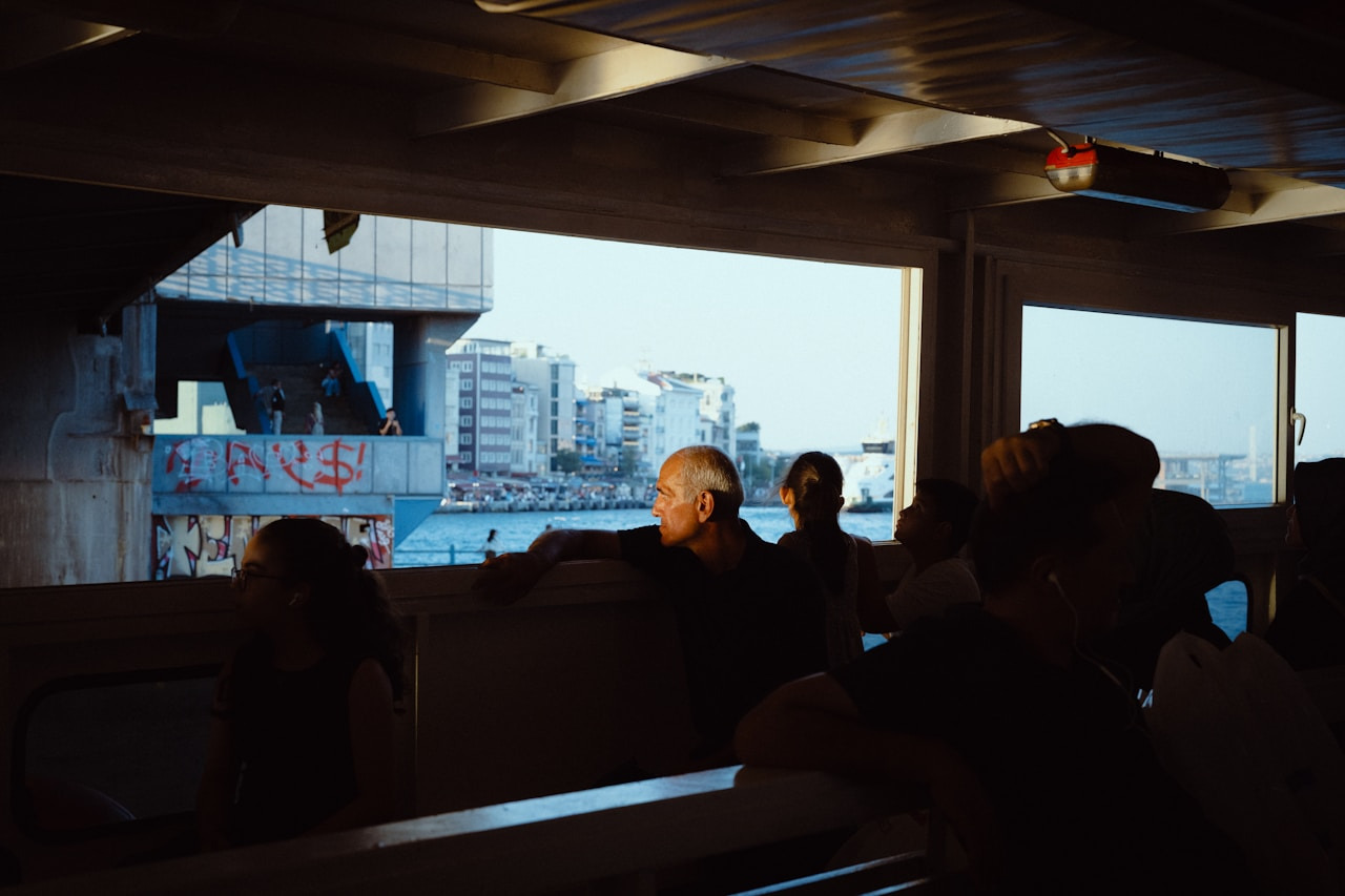 People looking out from a ferry window at a city waterfront with graffiti, Ultra