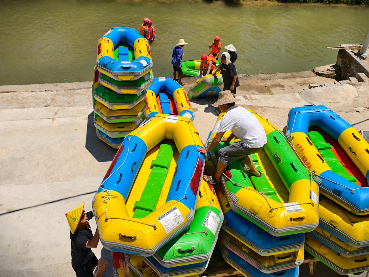 People preparing colorful inflatable rafts on a concrete riverbank for a rafting trip, Ultra