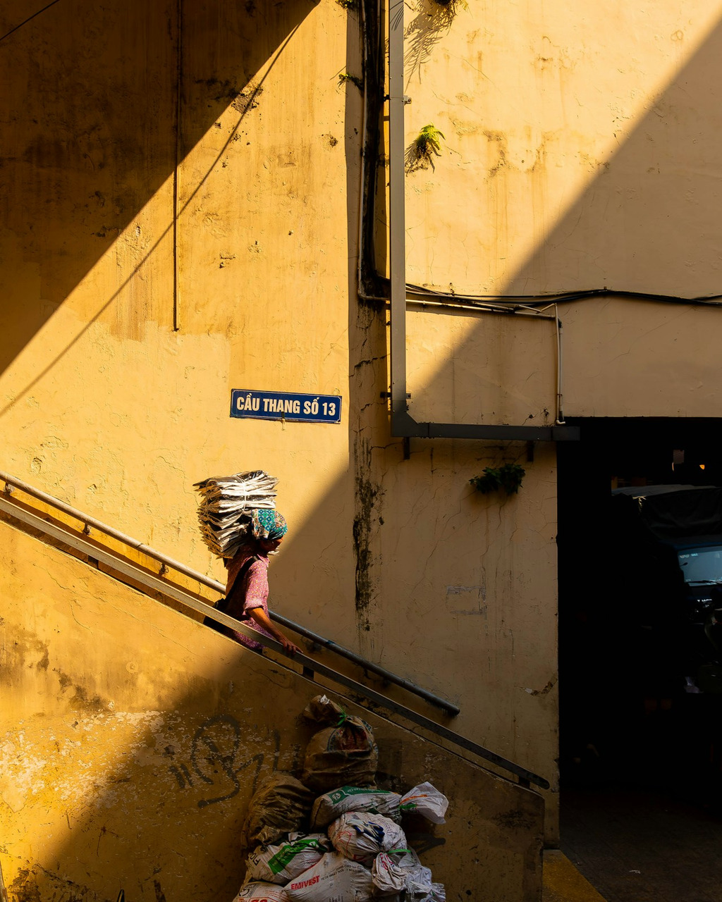 Person carrying a large bundle walks up sunlit yellow stairs, Ultra