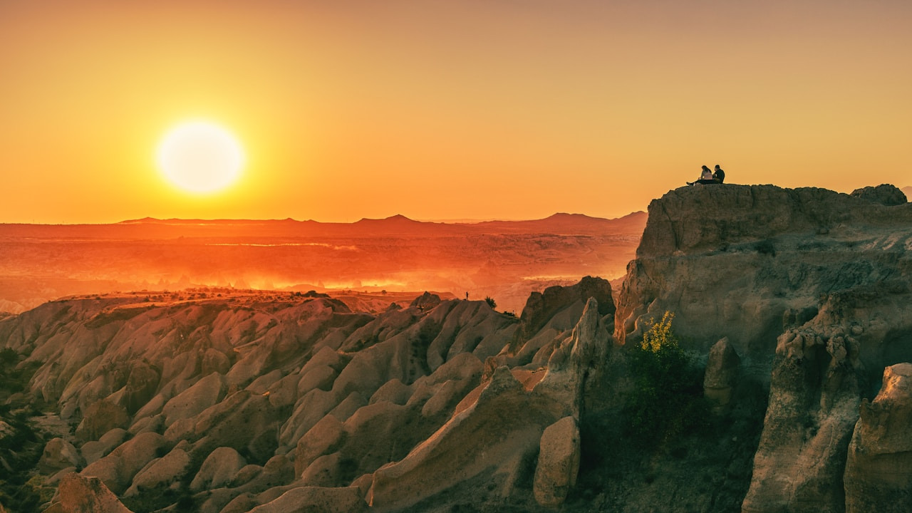 Two people on a rocky cliff overlooking a valley under a low sun, Ultra
