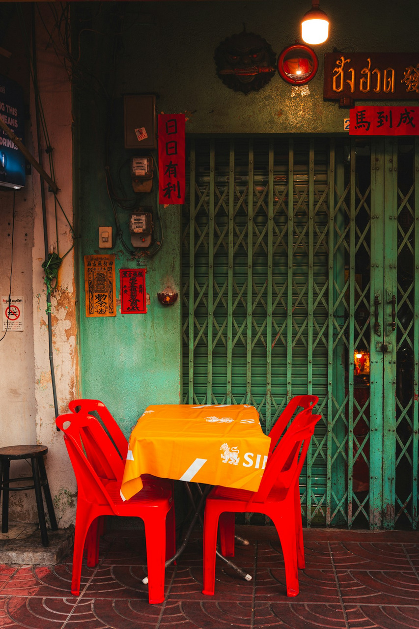 Two red plastic chairs at a table with an orange cloth before a green gate, Ultra