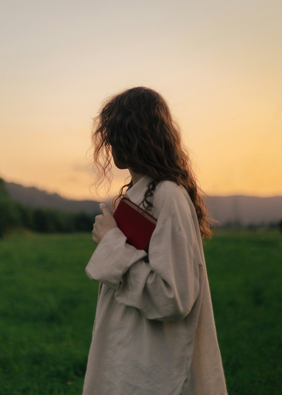 Woman holding a red book in a field at sunset, Ultra